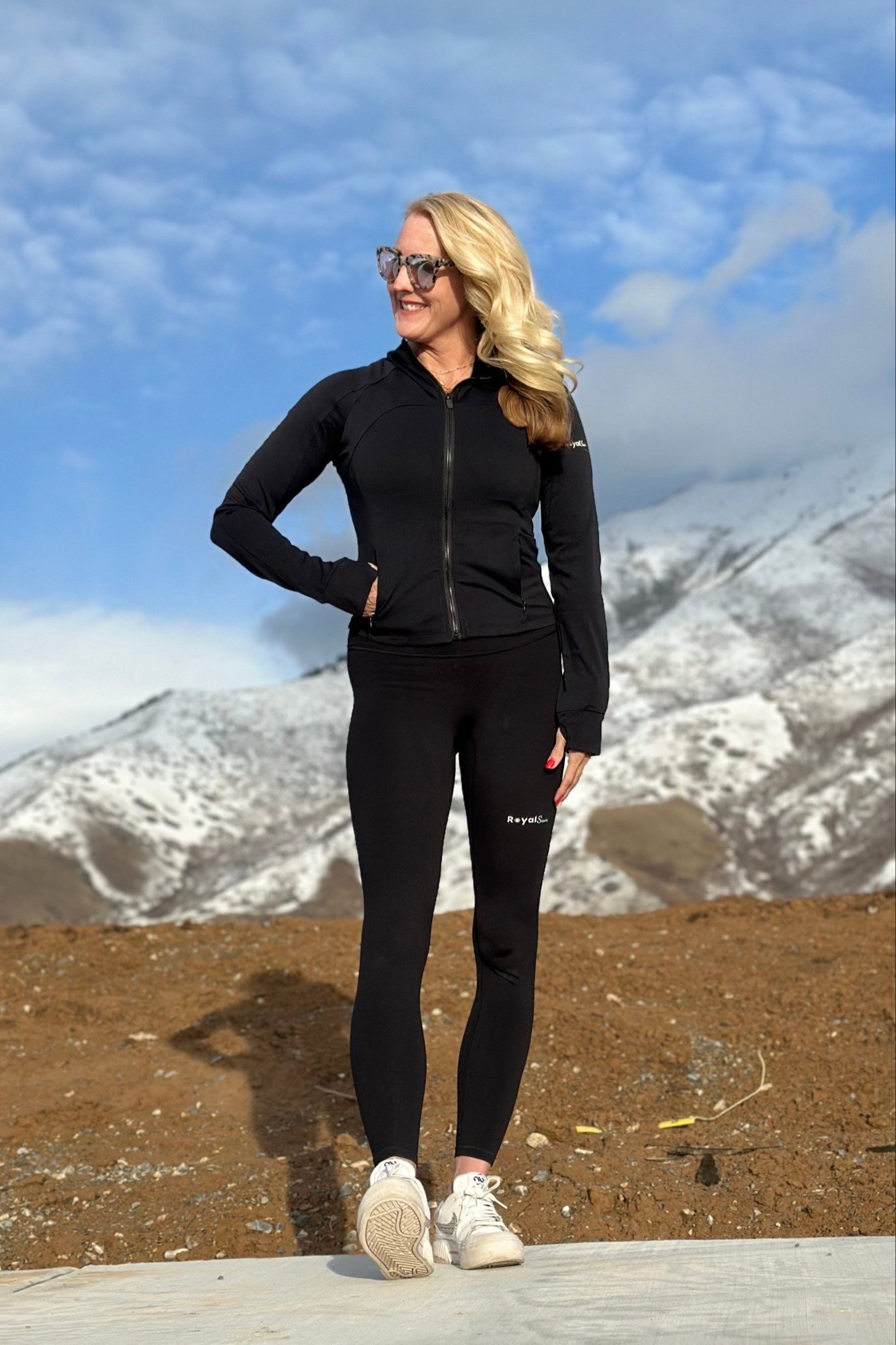 Woman in black athletic wear standing in a mountainous landscape with snow-capped peaks.